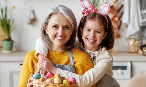 Lächelnde Großmutter mit Enkelin in Osterstimmung – gemeinsam bunte Eier bemalen und den April genießen.